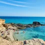 Caló des Mort, hidden cove in Formentera with reddish rocks and turquoise water under clear skies.